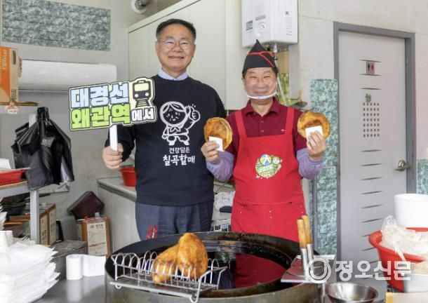 김재욱 칠곡군수(왼쪽)가 ‘대경선 왜관역에서’라는 문구가 적힌 팻말을 들고 웰빙왕호떡을 홍보하고 있다. 대경선을 타고 왜관역에 내려 호떡을 즐길 수 있다는 의미를 담은 촬영 장면.